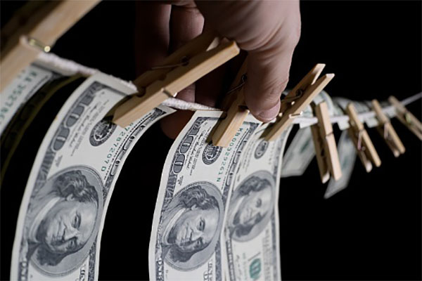 man's hand hangs dollars on a black background using clothespins on a rope. concept of dirty money.