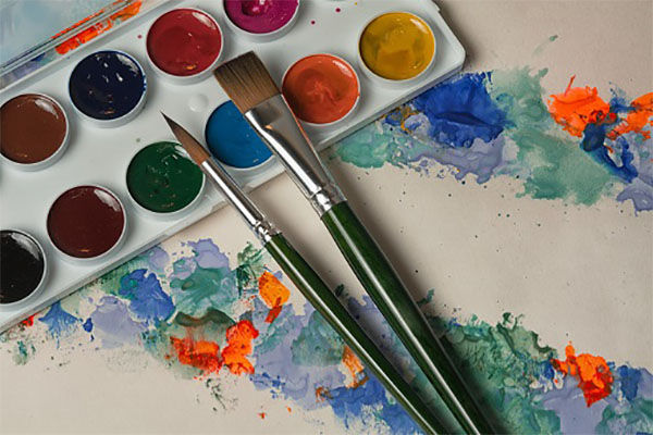 Plastic palette with colorful paints and brushes on painted paper background, top view with copy space